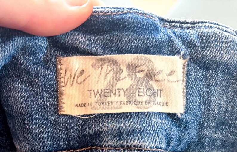 May include: Close-up of a denim garment with a label that reads "We The Free Twenty Eight." The label is stitched onto the blue fabric. The text "Made in Turkey / Fabriqu&eacute; en Turquie" is also visible.