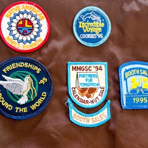 May include: A collection of embroidered patches with various designs and text. One patch reads "Native American" with a colorful sun design. Other patches include "Friendships Around the World," "Incredible Voyage," and "Booth Sales 1995."
