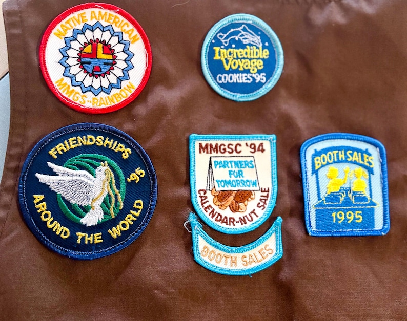 May include: A collection of embroidered patches with various designs and text. One patch reads "Native American" with a colorful sun design. Other patches include "Friendships Around the World," "Incredible Voyage," and "Booth Sales 1995."