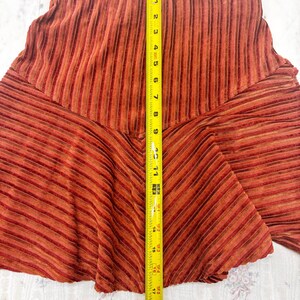 May include: A rust-colored skirt with vertical and diagonal stripes. The skirt is measured with a yellow tape measure, showing a length of approximately 19 inches. The fabric has a textured appearance.