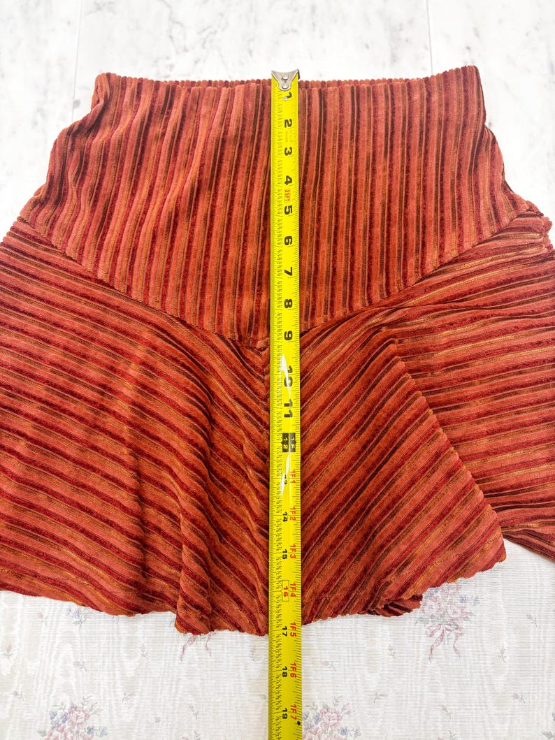 May include: A rust-colored skirt with vertical and diagonal stripes. The skirt is measured with a yellow tape measure, showing a length of approximately 19 inches. The fabric has a textured appearance.