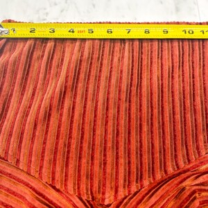 May include: Close-up of a section of orange and brown striped fabric. A yellow tape measure shows the width of the fabric is approximately 11 inches. The fabric has a textured, corduroy-like appearance.