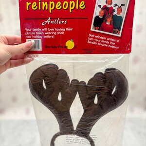 May include: A package of brown reindeer antlers on a headband. The packaging is red with the text "Santa's reinpeople Antlers". The package also includes a photo of children wearing the antlers. One size fits all.