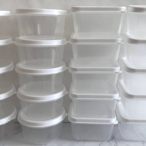以下が含まれることがあります： 白い蓋が付いた透明なプラスチック容器が18個セットになっています。容器は3列6個ずつ積み重ねられています。容器はすべて同じサイズと形であり、すべて空です。