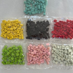 以下が含まれることがあります： 発泡スチロール製のカラフルな小さな幾何学模様の6つの袋。袋は透明なプラスチック製で、形はターコイズ、黒、赤、緑、ピンク、グレーです。