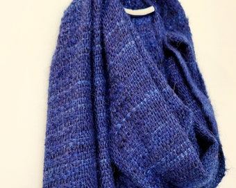 May include: A blue knitted scarf with a textured weave. The scarf is folded and draped over a white surface.