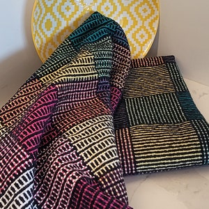 May include: A black and white striped fabric with colorful stripes in a rainbow pattern. The fabric is folded and draped over a yellow bowl with a white geometric pattern.