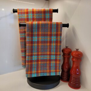 May include: Two red and blue plaid kitchen towels hanging on a black towel rack with two salt and pepper shakers on a counter.