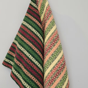 May include: Two kitchen towels with a striped pattern in shades of green, red, and cream. The towels are hanging on a hook.