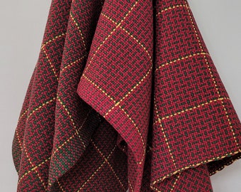 May include: A red, green, and yellow plaid kitchen towel hangs on a hook. The towel is folded in half and has a woven pattern.