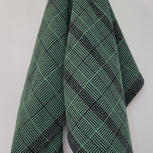 May include: A green and black patterned fabric handkerchief. The fabric has a woven design with a geometric pattern.