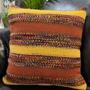 Puede incluir: Una almohada de tiro de rayas amarillas, naranjas y marrones con un patrón tejido texturizado.