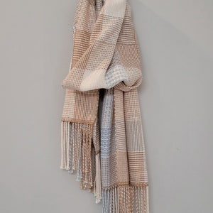 May include: A woven scarf with a checkered pattern in shades of brown, beige, and blue. The scarf has fringe on the ends.