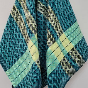 May include: A teal blue kitchen towel with a white and yellow checkered pattern. The towel is folded and hanging on a white wall.
