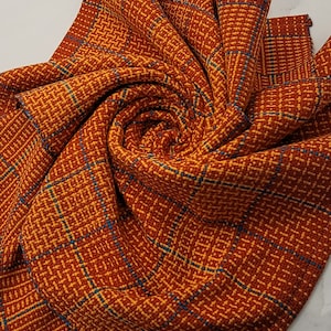 May include: A red and yellow plaid fabric with a blue woven pattern. The fabric is folded into a spiral shape.