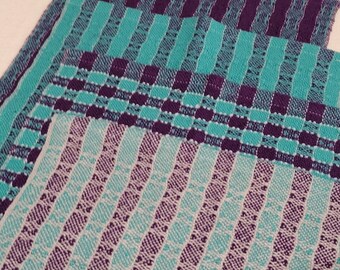 May include: Three woven fabric tea towels in shades of teal and purple. The towels have different patterns, including stripes and a checkered pattern.
