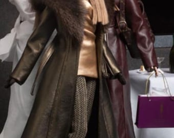 Può includere: Tre bambole di moda che indossano eleganti cappotti invernali. La bambola al centro indossa un cappotto di pelle marrone con colletto di pelliccia e una maglia dorata. La bambola a sinistra indossa una camicia bianca e la bambola a destra indossa un cappotto di pelle bordeaux.