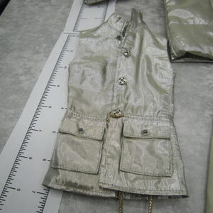 Pu&ograve; includere: Un gilet color argento con due tasche frontali e bottoni decorativi. Il gilet ha un colletto alto e una catena color oro. &Egrave; visibile anche una giacca argentata abbinata.