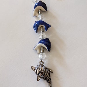 May include: A silver chain with a silver dolphin charm and three blue and white ceramic dolphin charms. The charms are strung on a silver wire with clear crystal beads.