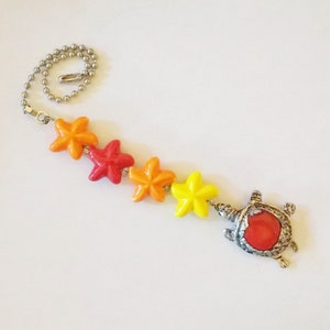 May include: A silver chain with a red, orange, and yellow star-shaped bead charm and a silver turtle charm with a red gem.