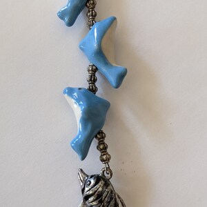 Puede incluir: Una cadena plateada con cuatro dijes de delfín de cerámica azul y un dije de delfín de metal plateado en la parte inferior.