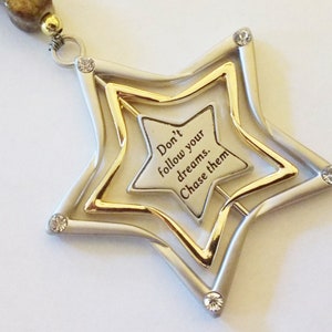 May include: A silver and gold star-shaped pendant with rhinestones. The pendant has the inscription "Don't follow your dreams. Chase them."