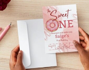 以下が含まれることがあります： ドーナツのグラフィックと「The Sweet One」と「Saig's First Birthday」のテキストが書かれたピンクと白の招待状。