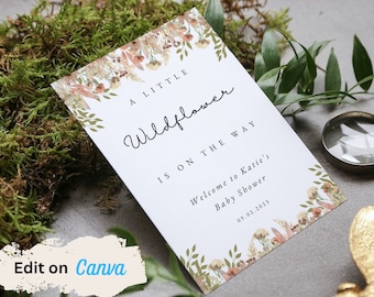 以下が含まれることがあります： 花柄のデザインが施された白いカードに、「A Little Wildflower Is On The Way」と「Welcome to Katie's Baby Shower 09.02.2023」の文字が書かれています。