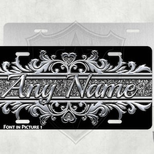 May include: Black and silver personalized license plate with a decorative silver scroll design and the text "Any Name" in a sparkly silver font.