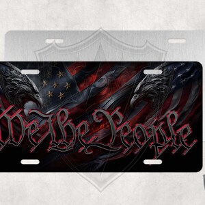 May include: A black and red license plate featuring a stylized American flag with the words "We the People" in a bold, gothic font.