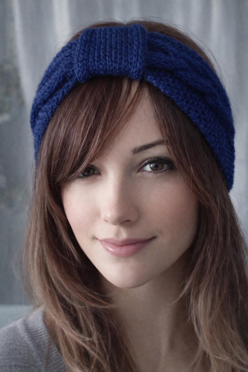 May include: A close-up of a woman wearing a knitted blue headband. The headband is a solid, vibrant blue color and has a textured appearance. The woman has long, light brown hair and is looking at the camera.