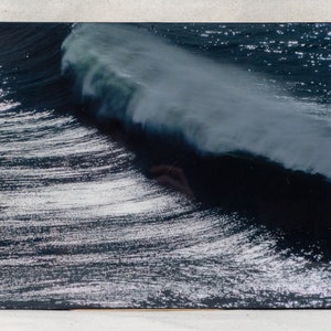 May include: A close-up photograph of a large wave crashing in the ocean. The wave is white and foamy, and the water is dark blue. The sun is shining on the water, creating a sparkling effect.