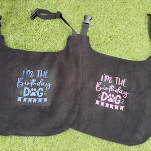 Könnte beinhalten: Zwei schwarze Hundewesten mit verstellbaren Trägern. Eine Weste hat blauen Text, der "Ich bin der Geburtstagshund" mit einem Pfotenabdruck und Girlanden sagt. Die andere Weste hat rosa Text, der "Ich bin der Geburtstagshund" mit einem Pfotenabdruck und Girlanden sagt.