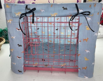 May include: A blue dog print fabric dog crate cover with black ribbon ties. The crate is pink metal.