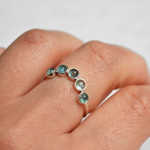 May include: A silver ring with a row of six light blue gemstones set in a curved shape.