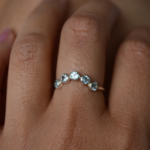 May include: A silver ring with a row of six light blue gemstones set in a curved shape.