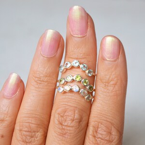 May include: Three silver rings with different coloured gemstones. The top ring has light blue gemstones, the middle ring has green gemstones, and the bottom ring has white gemstones.