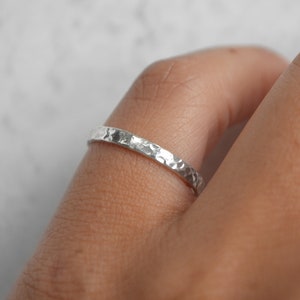 May include: A silver hammered ring worn on a finger.