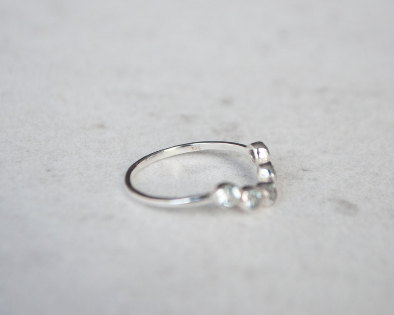 May include: A silver ring with a row of small, round stones set in a curved design.