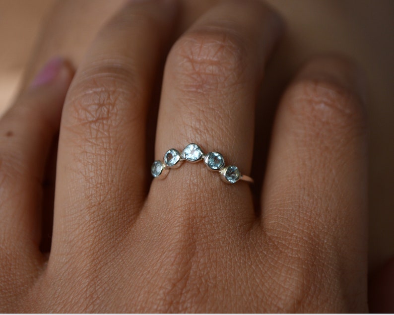 May include: A silver ring with a row of six light blue gemstones set in a curved shape.
