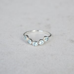 May include: A silver ring with a row of six light blue gemstones set in a curved shape.