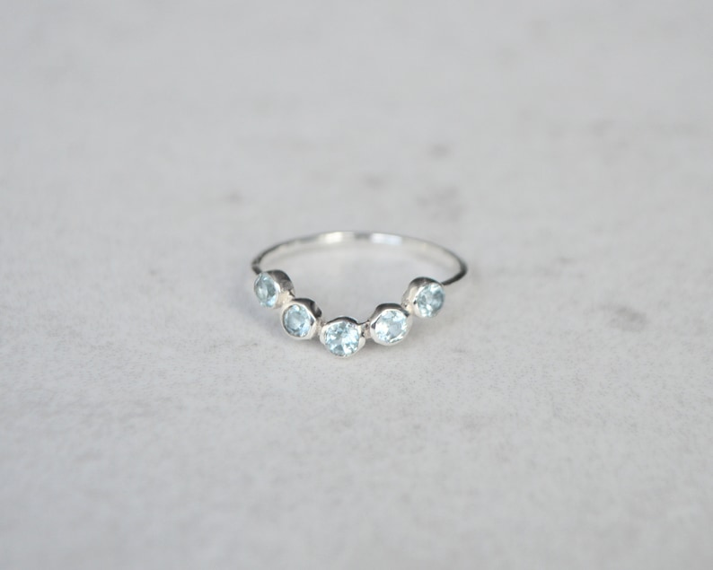 May include: A silver ring with a row of six light blue gemstones set in a curved shape.