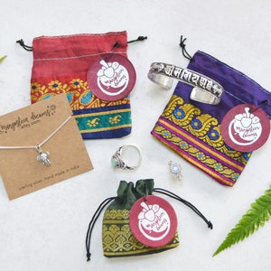 May include: Jewelry items including a silver bracelet, rings, and a necklace with an elephant pendant are displayed with colorful drawstring bags. The bags have tags with a logo and the text "mangosfeer dreams etsy.com". The necklace card reads "sterling silver, hand made in india".