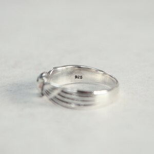 May include: A silver ring with a small, round gemstone. The ring has a textured design on the band and the number "925" is stamped inside the band. The ring is set against a white background.