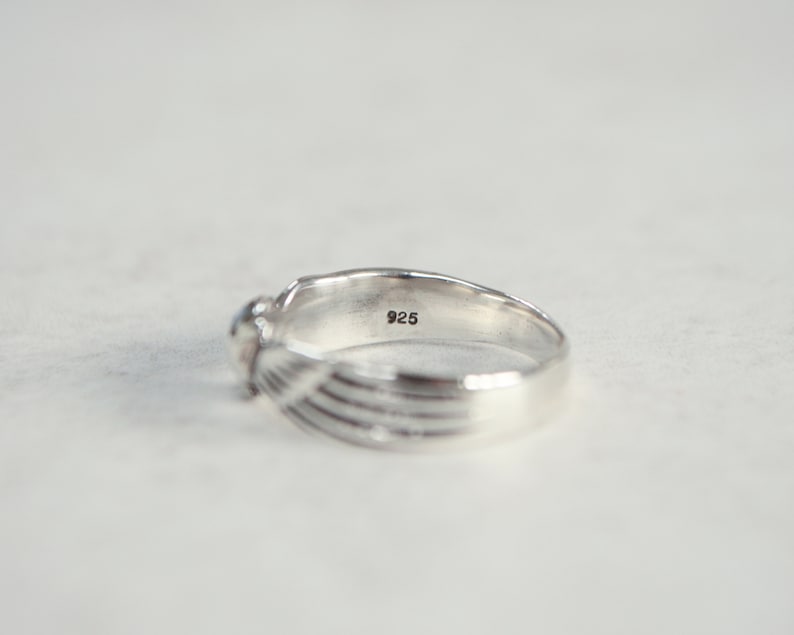 May include: A silver ring with a small, round gemstone. The ring has a textured design on the band and the number "925" is stamped inside the band. The ring is set against a white background.