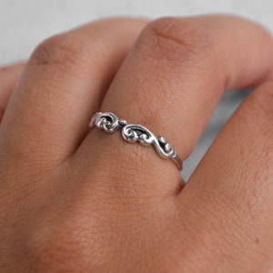 May include: A silver ring with a delicate, swirling design. The ring is worn on a finger.