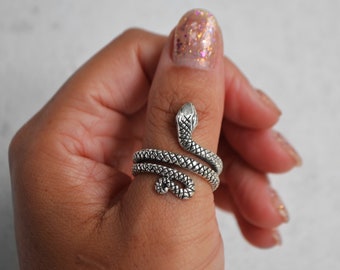 Puede incluir: Un anillo de serpiente de plata con un diseño en espiral. El anillo se lleva en el pulgar.