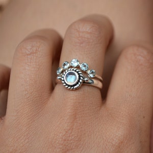 May include: A silver ring set with a large round moonstone and a smaller band of five round clear stones.