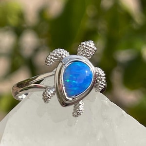 May include: A silver ring featuring a blue opal set in a turtle design.