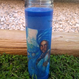 May include: Blue glass candle with a blue wax layer and a label featuring a woman with a blue head wrap and seashells. The label text reads "Spellangelemporium".